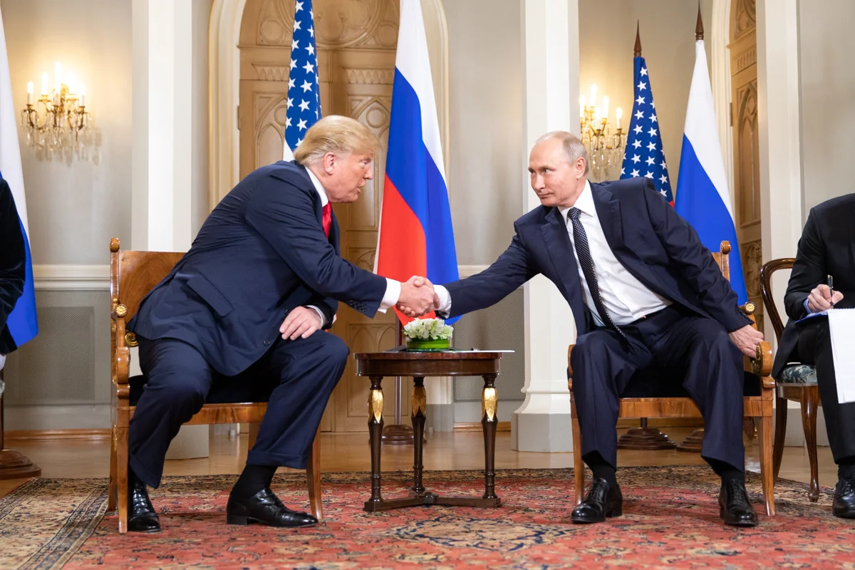 Donald Trump and Vladimir Putin shake hands while seated in Helsinki on July 16, 2018, with U.S. and Russian flags behind them.