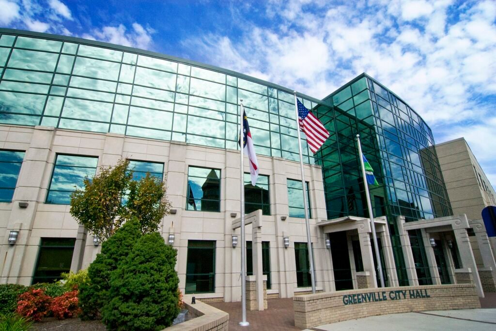 Greenville City Hall in North Carolina with American, state and city flags outside the glass-fronted building